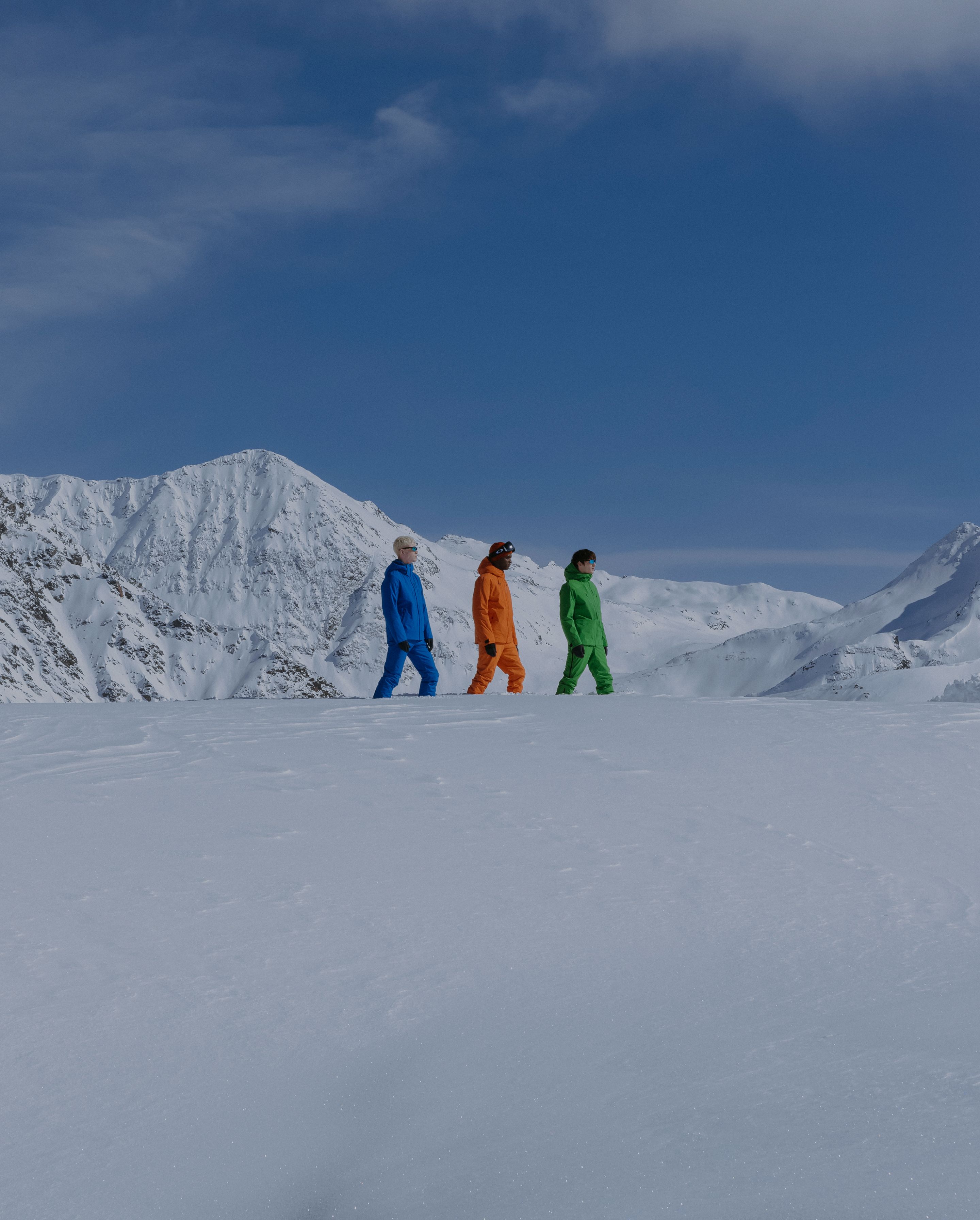 Shooting tre uomini con tuta sulla neve, blu arancio e verde