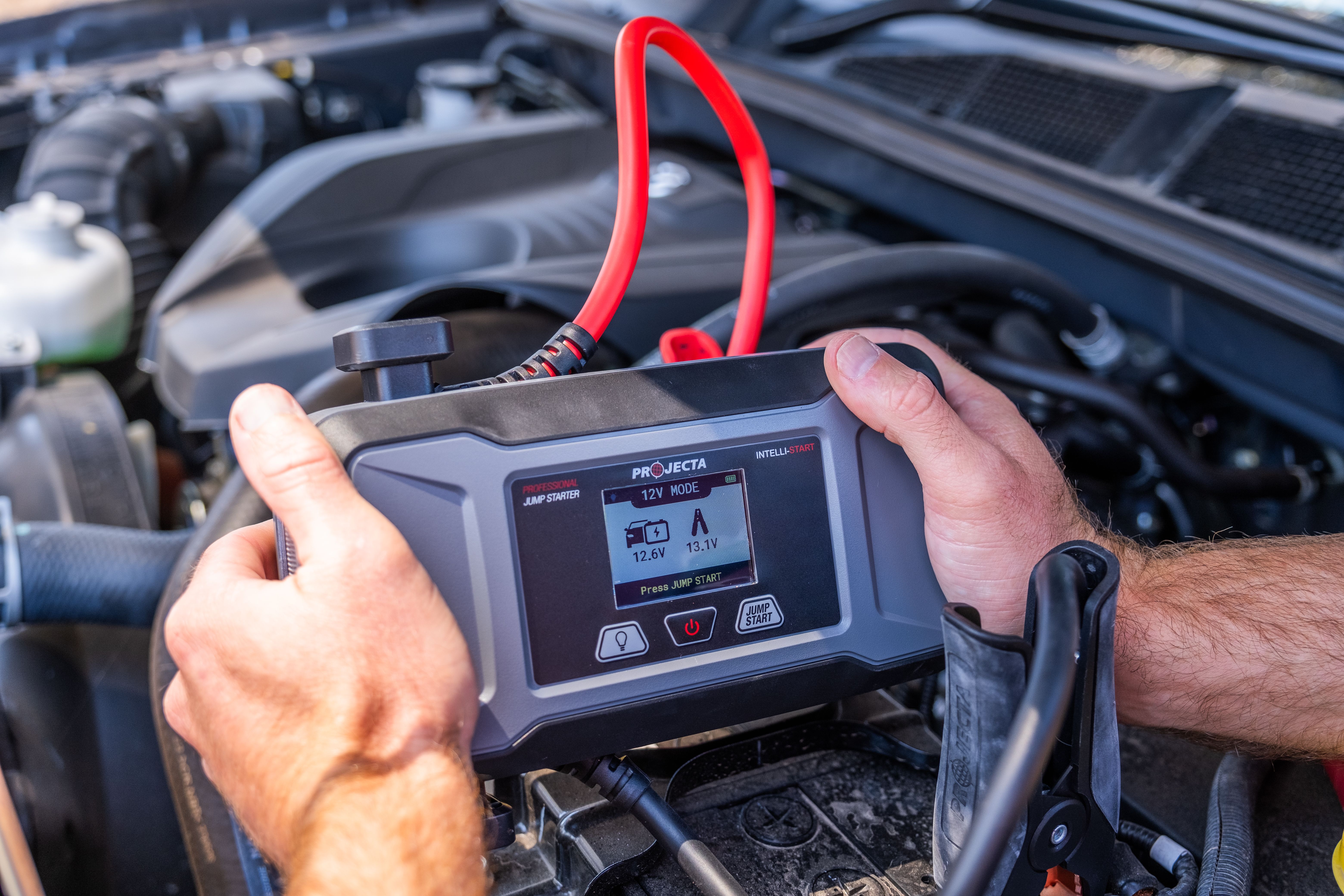 Hands holding a Projecta Intelli-Start professional jump starter in an engine bay
