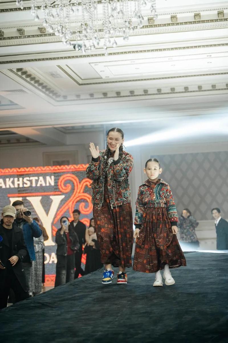 Banu Gaidar applauds on the runway at the end of the show, a girl in a BAY bomber beside her