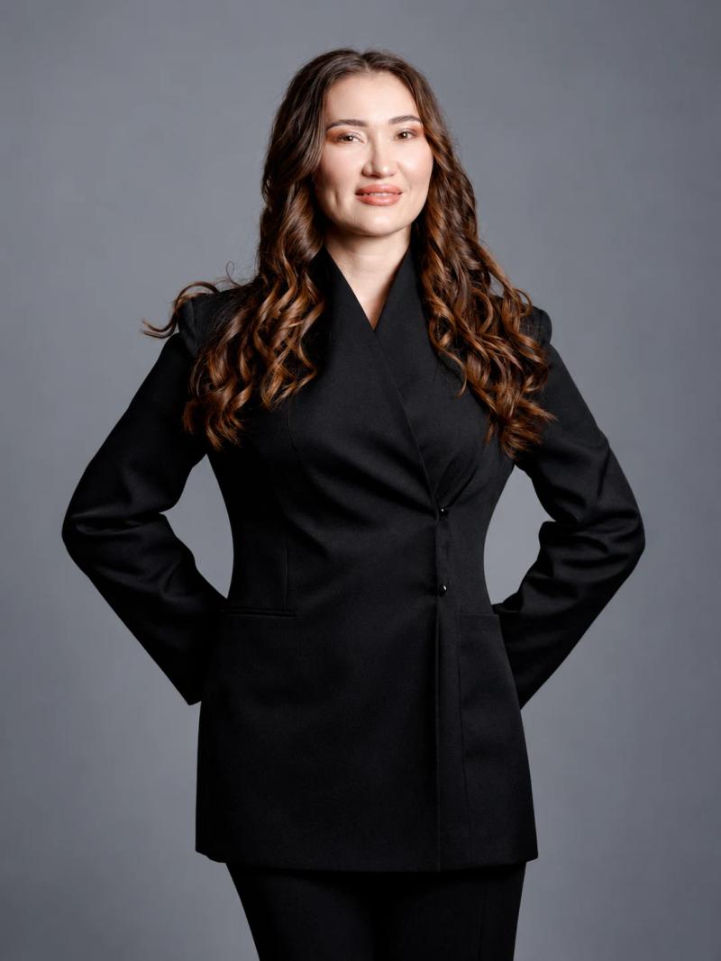 Banu Gaidar in a black suit on a grey background, studio portrait