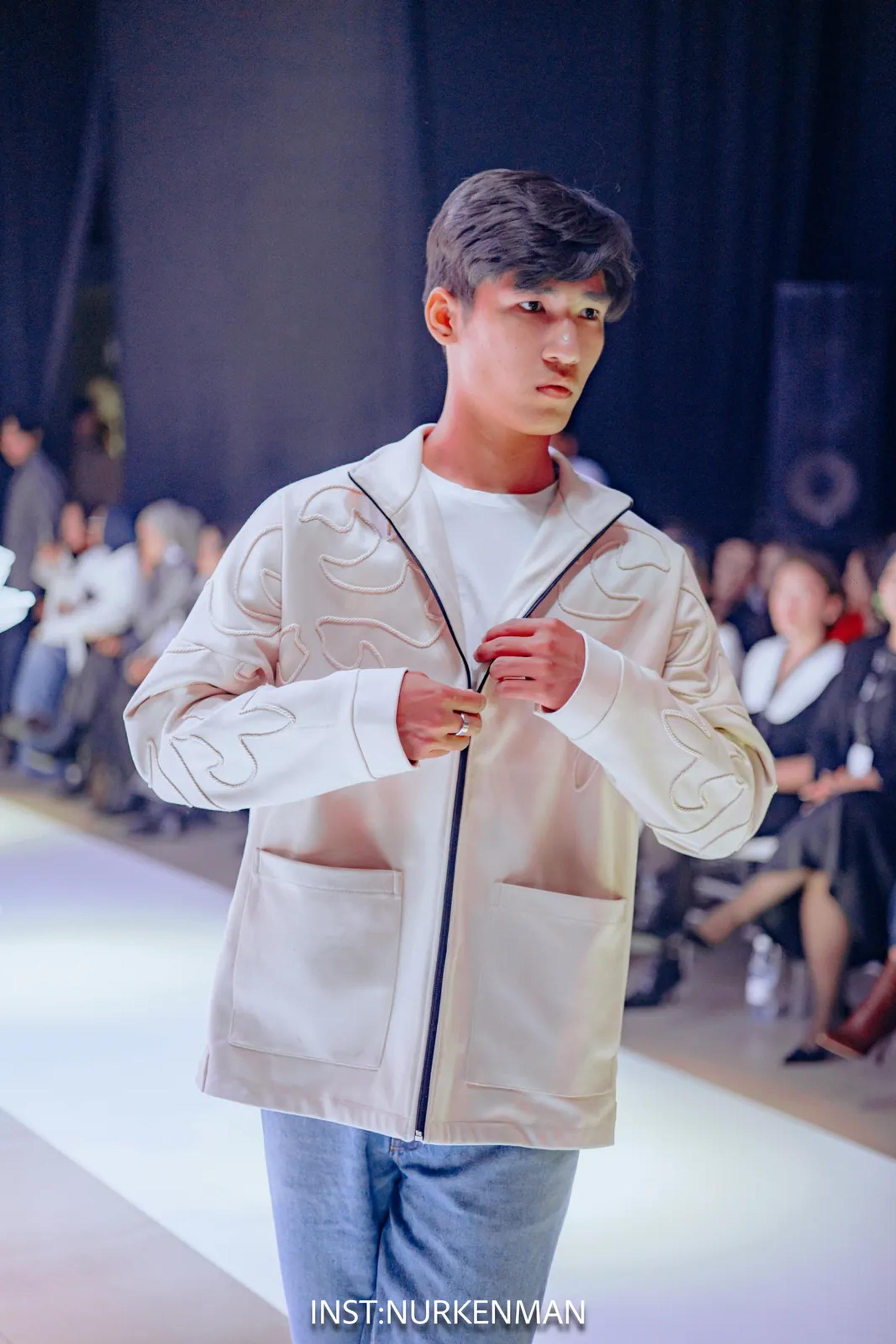 Model in a cream jacket with corded ornament on the runway