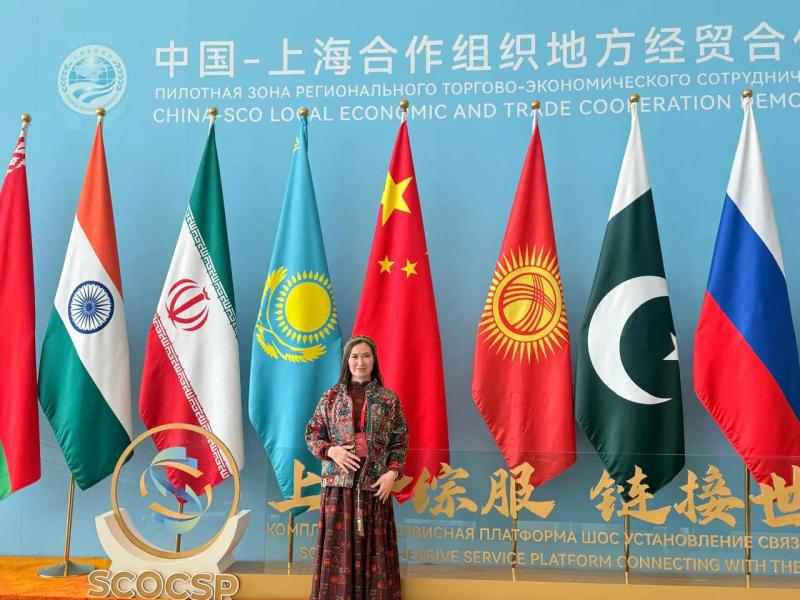 Banu Gaidar in front of the flags at the China–SCO local economic and trade cooperation demonstration area