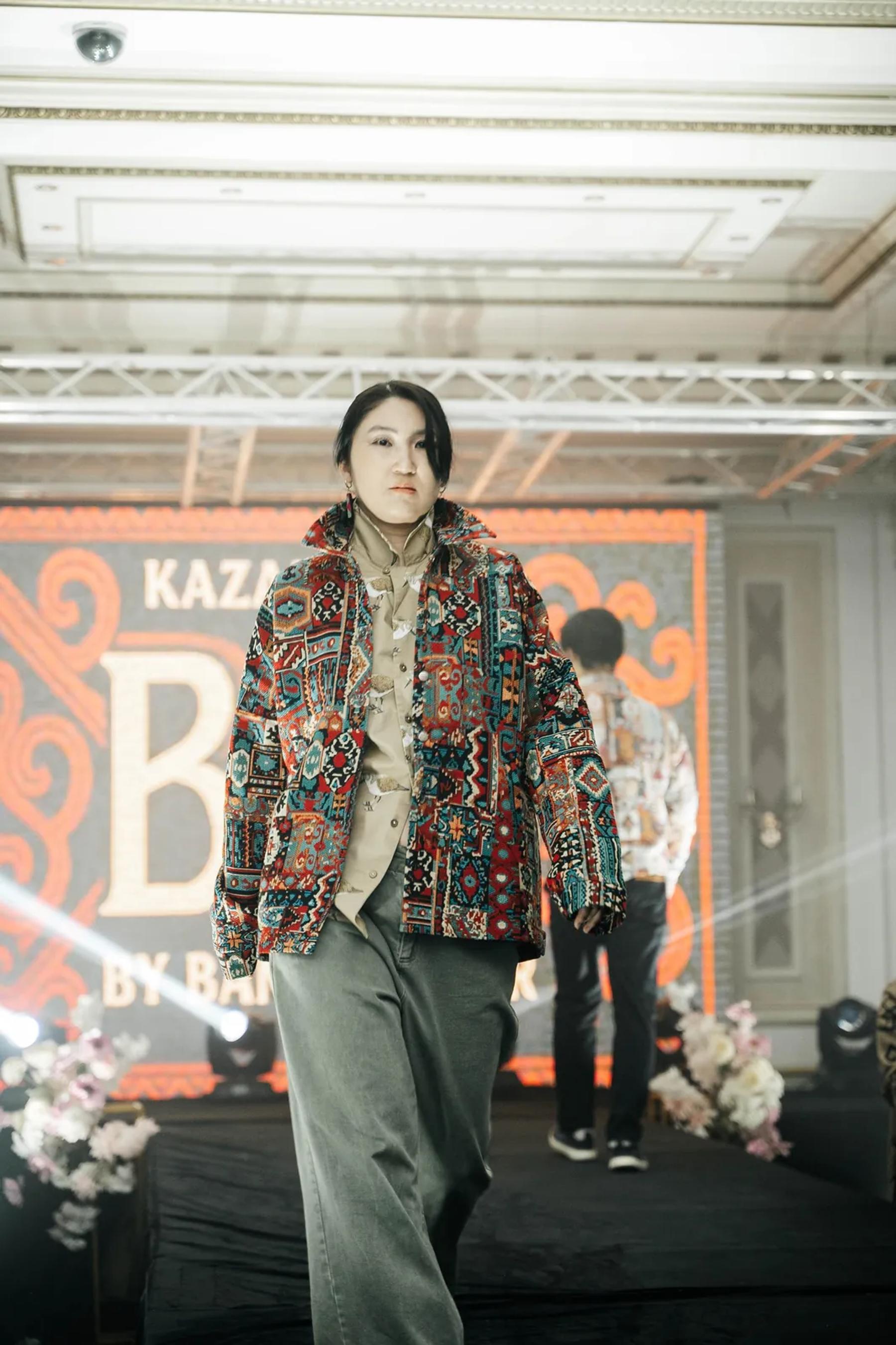 Model in a BAY bomber on the runway, the BAY by Banu Gaidar logo on the screen