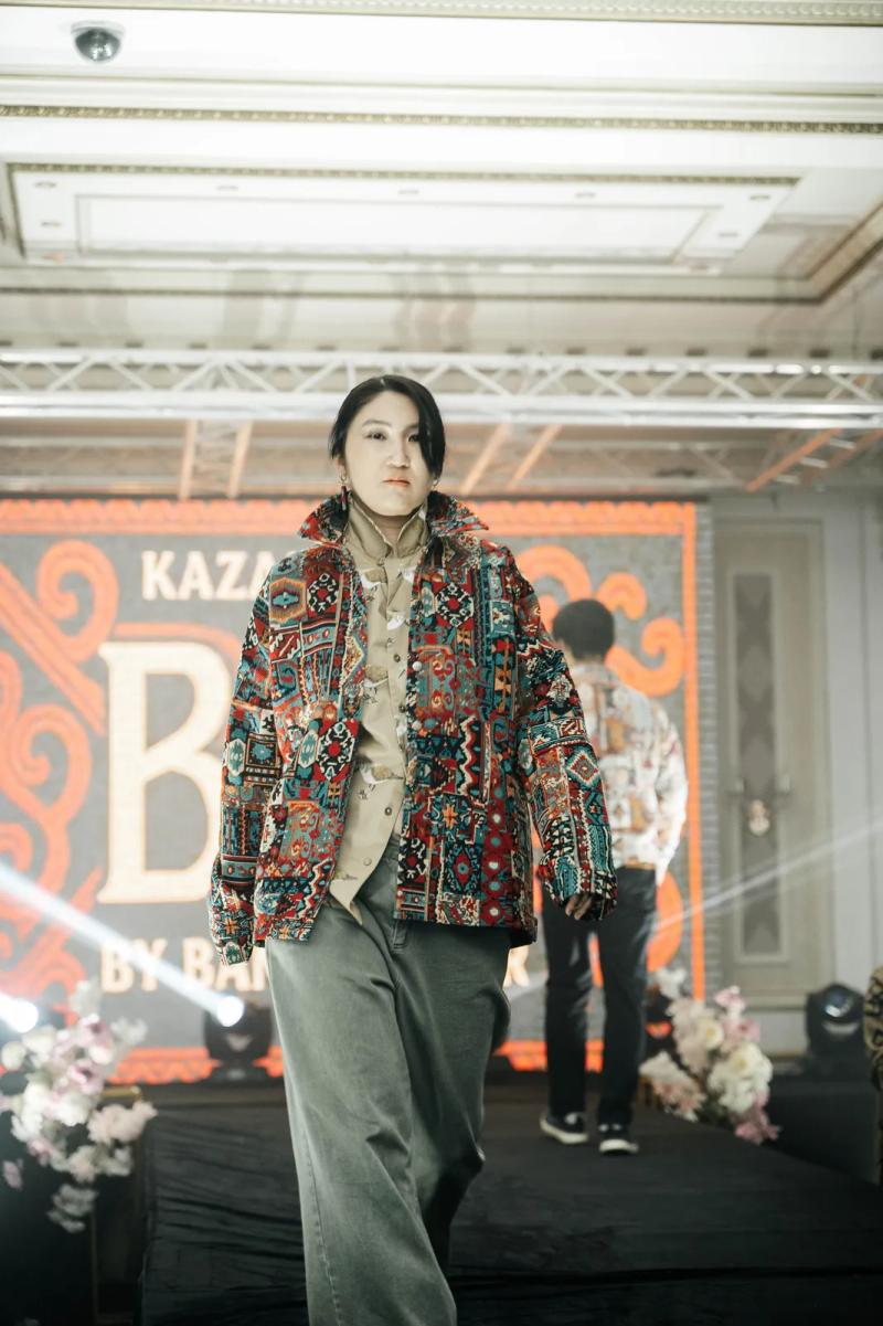Model in a BAY bomber on the runway, the BAY by Banu Gaidar logo on the screen
