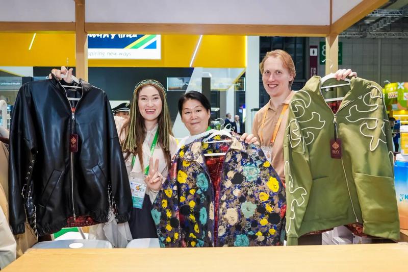 Banu Gaidar and visitors hold up BAY jackets at the stand
