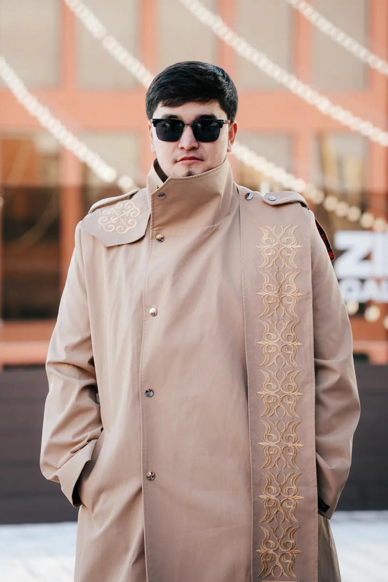 Model in a beige trench coat with embroidered ornament, outdoors