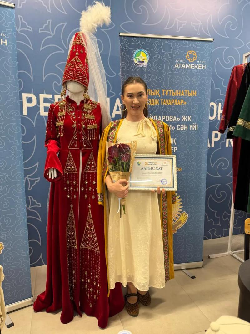 Banu Gaidar with a letter of thanks beside a national costume at an exhibition