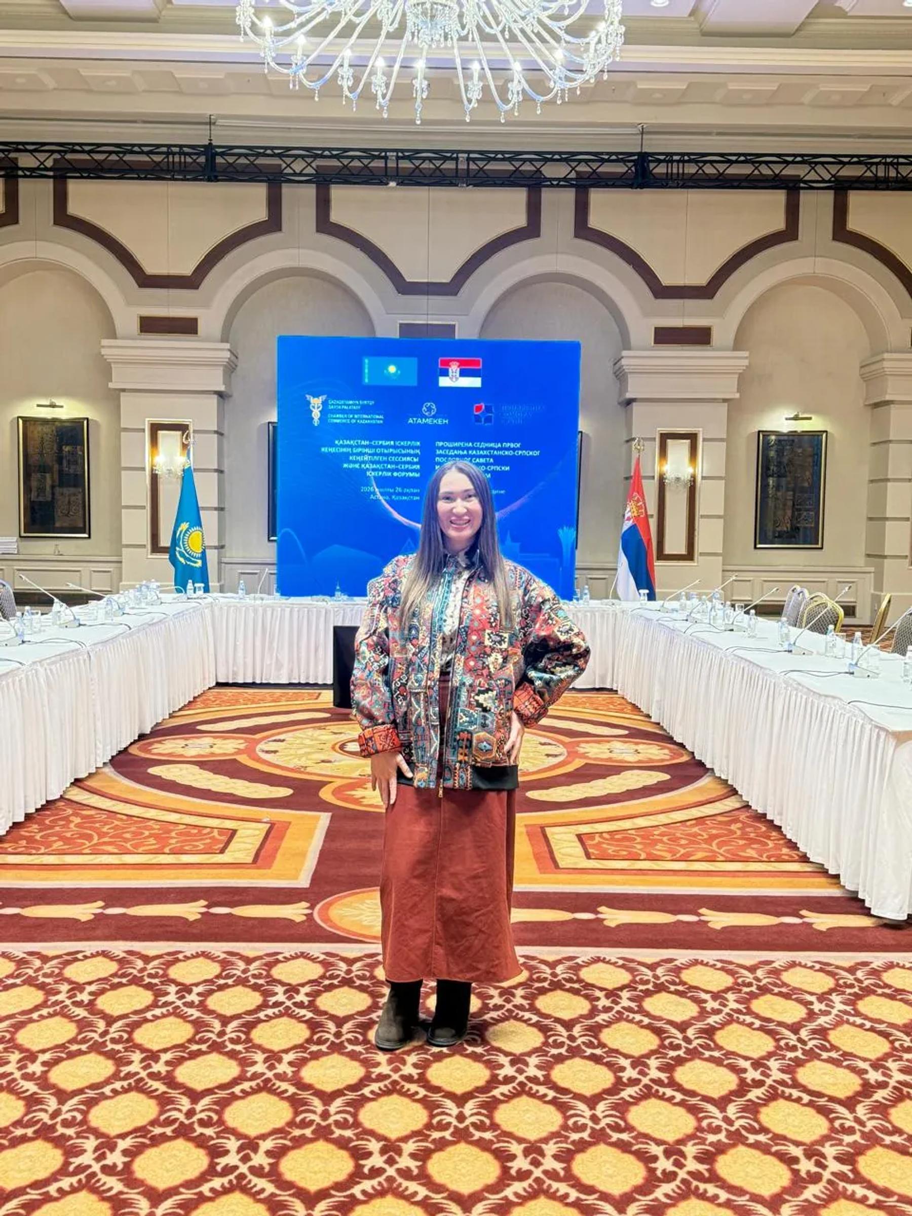 Banu Gaidar in the forum hall, the flags of Kazakhstan and Serbia behind her