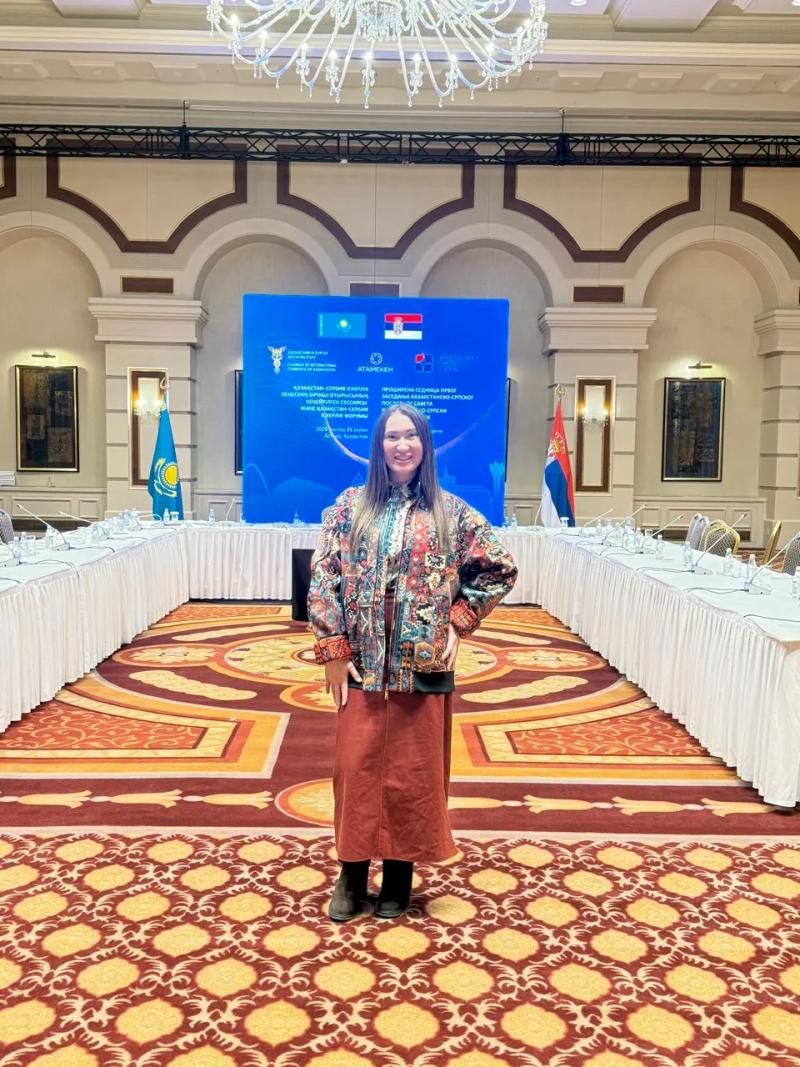 Banu Gaidar in the forum hall, the flags of Kazakhstan and Serbia behind her
