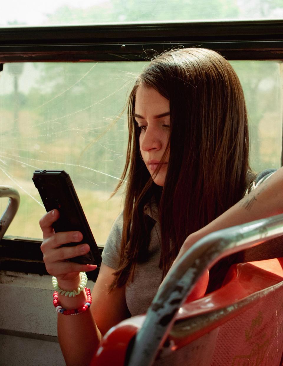 A young woman on a bus reading a message on her phone, brow drawn.
