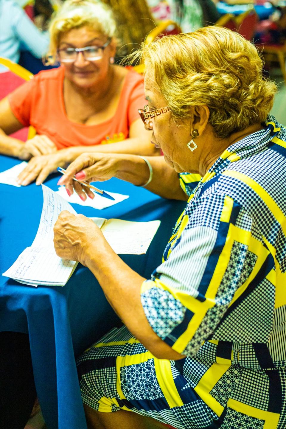 Two older residents at a community-hall table comparing handwritten notes.
