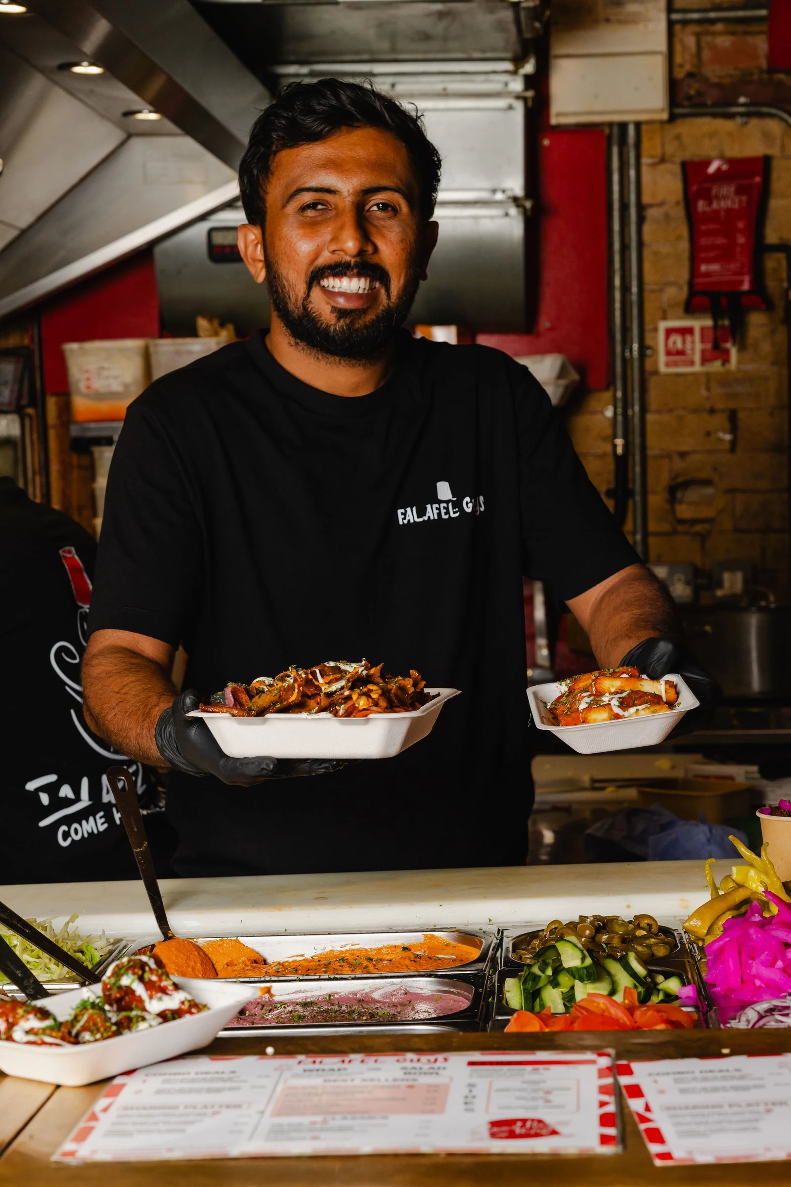 A smiling person holding prepared dishes behind a Northern Market food counter