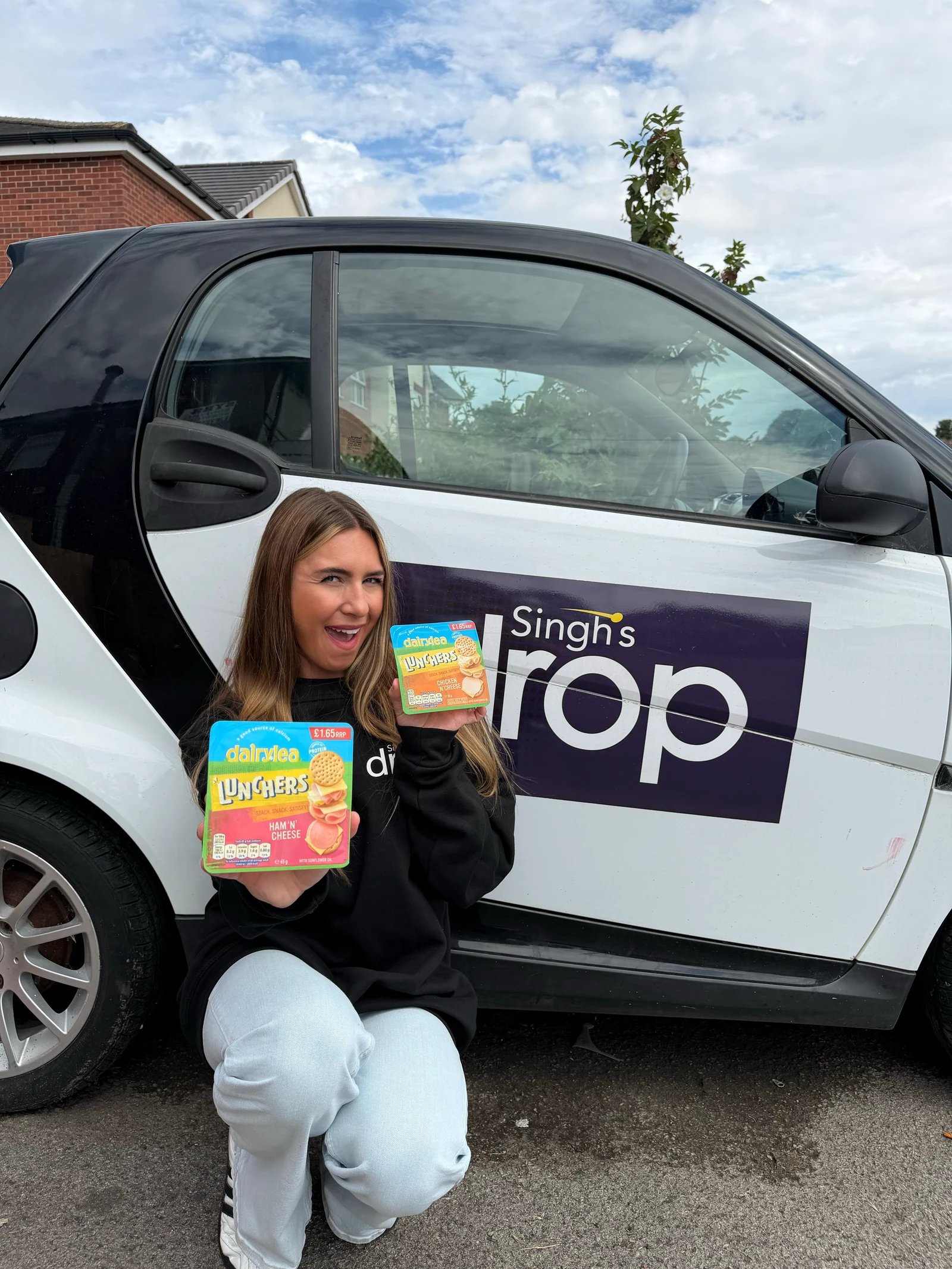 A presenter holding snack products beside a Singh's Drop branded delivery vehicle