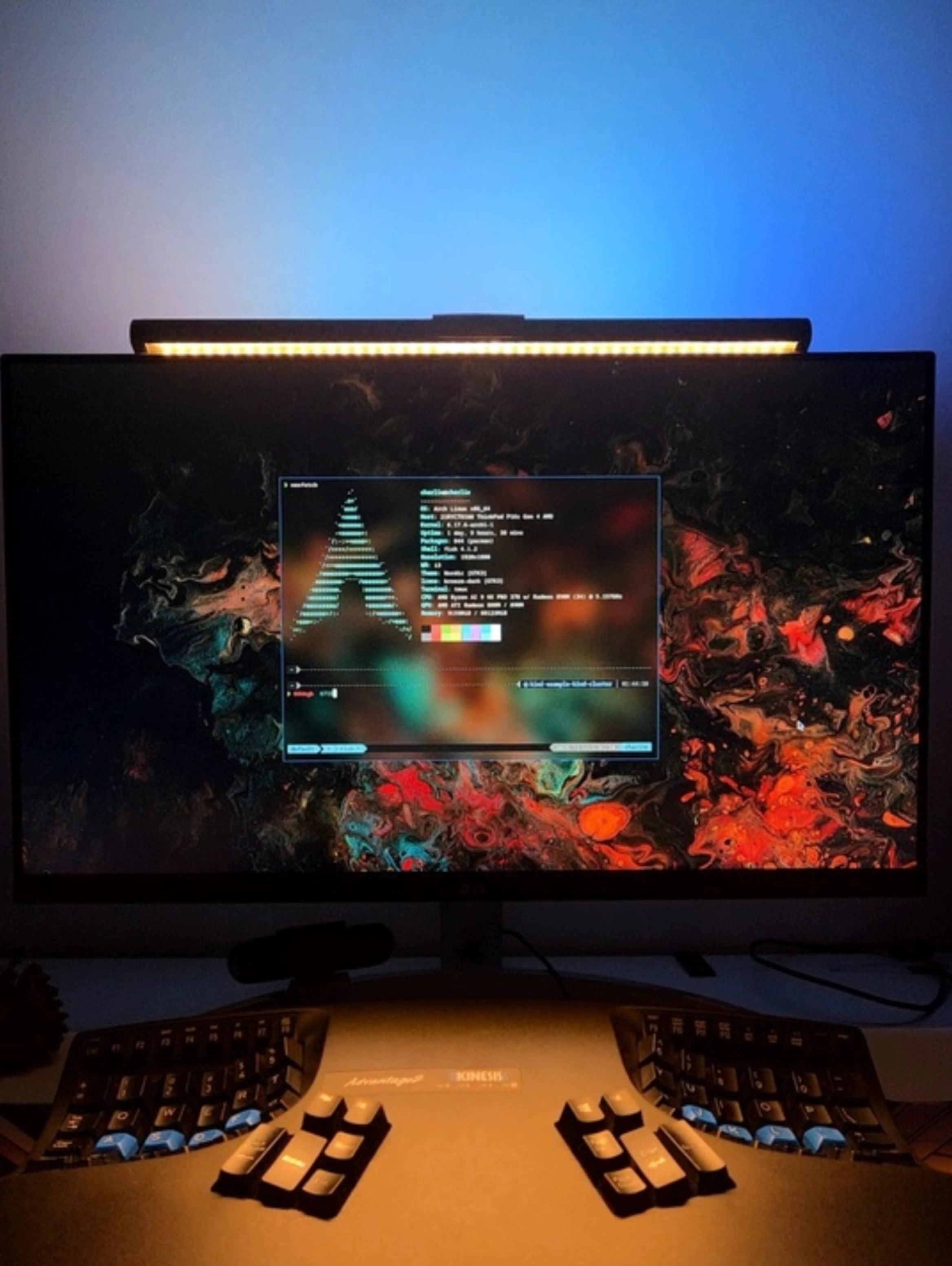 A moody, backlit desk setup featuring a widescreen monitor displaying the Arch Linux neofetch system information tool, showing system specs and an ASCII art Arch logo. The background is a colorful, marbled abstract wallpaper in shades of red, orange, teal, and black. A monitor light bar illuminates the space with a warm glow, contrasting against a soft blue-lit wall. In the foreground sits a Kinesis Advantage2 ergonomic keyboard with concave key wells and blue modifier keycaps, completing a focused and visually striking Linux development workstation.