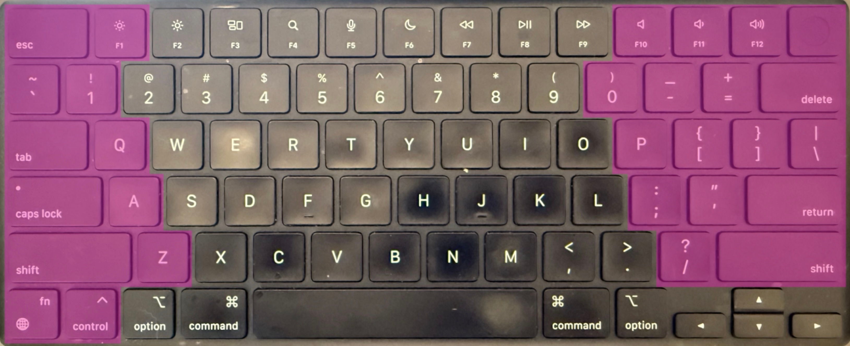 Overhead view of a black MacBook-style keyboard with visible wear on the central keys. The left and right sections of the keyboard — including modifier keys, punctuation, and function keys — are highlighted in purple, while the center keys remain uncolored. This highlights a split keyboard concept by isolating the hand zones. The layout includes standard QWERTY keys, macOS-specific modifiers like "command" and "option," and arrow keys in the bottom right.