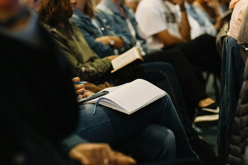 Congregation members seated in a row during a service, one following along in an open Bible