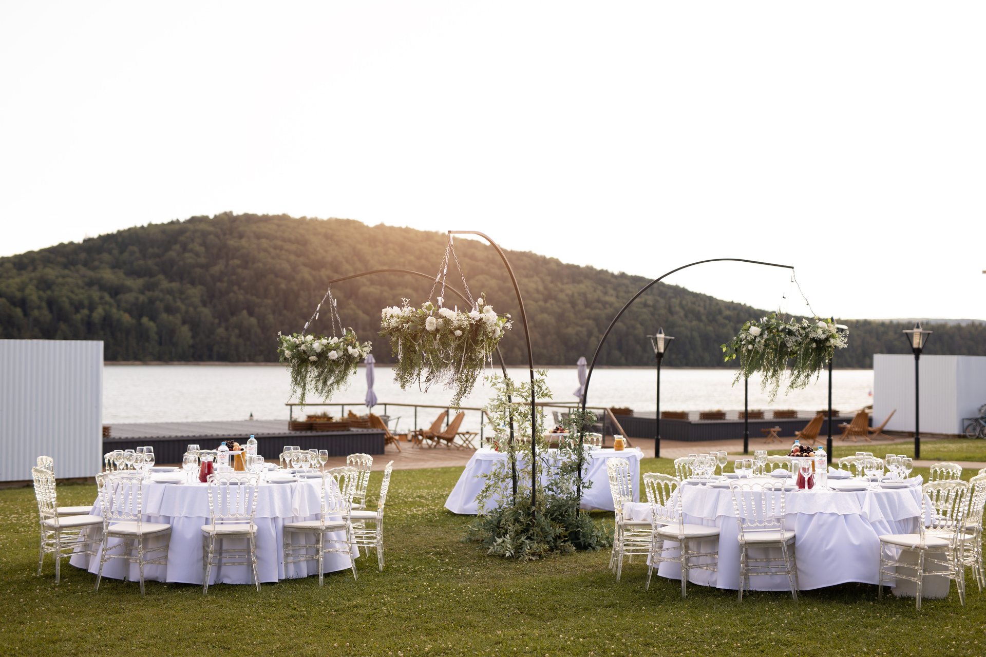 Banquet-style outdoor setup with round tables, white linens and chiavari chairs on grass