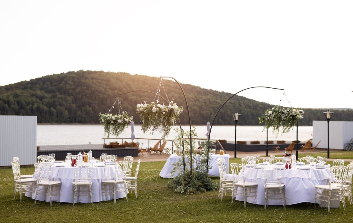 Banquet-style outdoor setup with round tables, white linens and chiavari chairs on grass