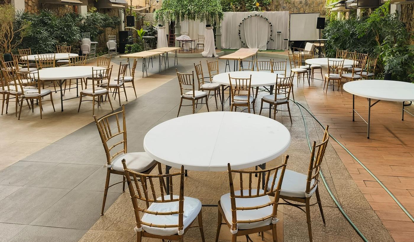 Empty elegant indoor venue setup with round tables and chairs, greenery, and soft lighting