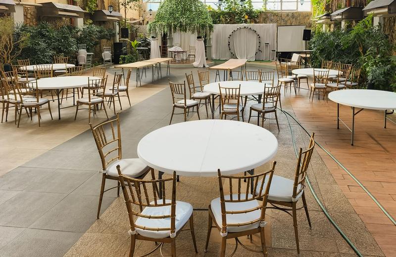 Empty elegant indoor venue setup with round tables and chairs, greenery, and soft lighting