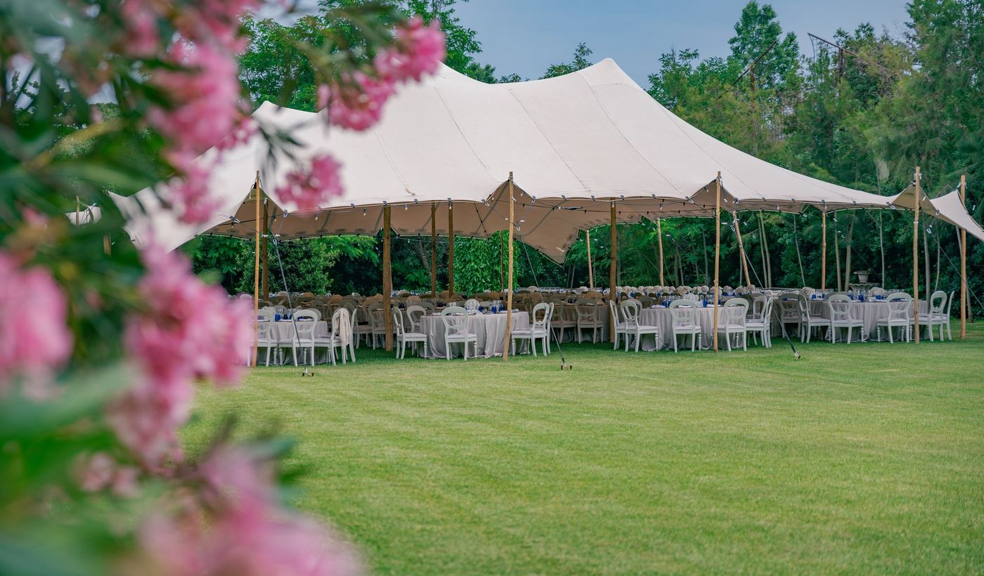 Outdoor event layout with round tables and white chairs set up under a tent on a lawn