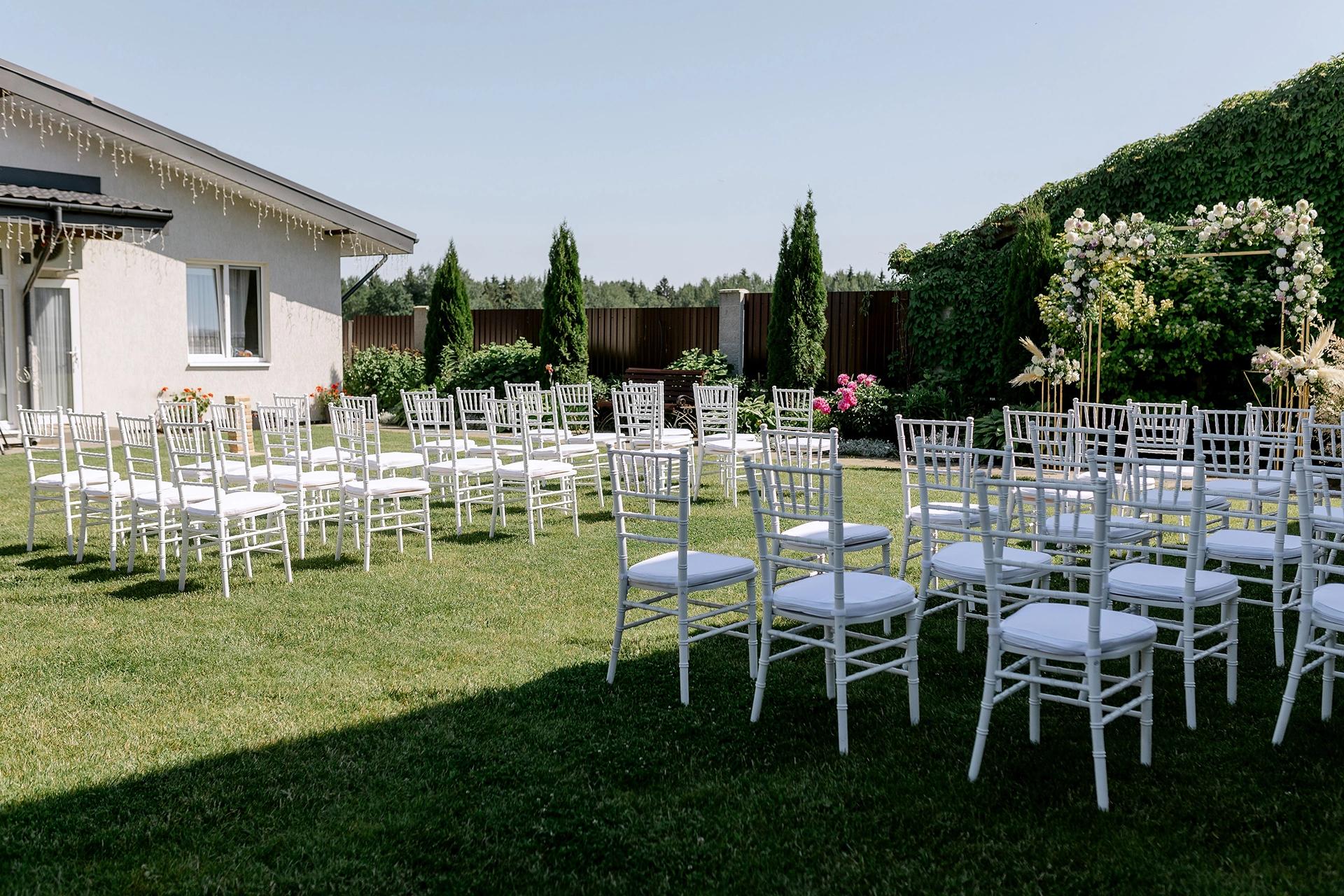 White chairs arranged in a garden setting for an outdoor wedding ceremony