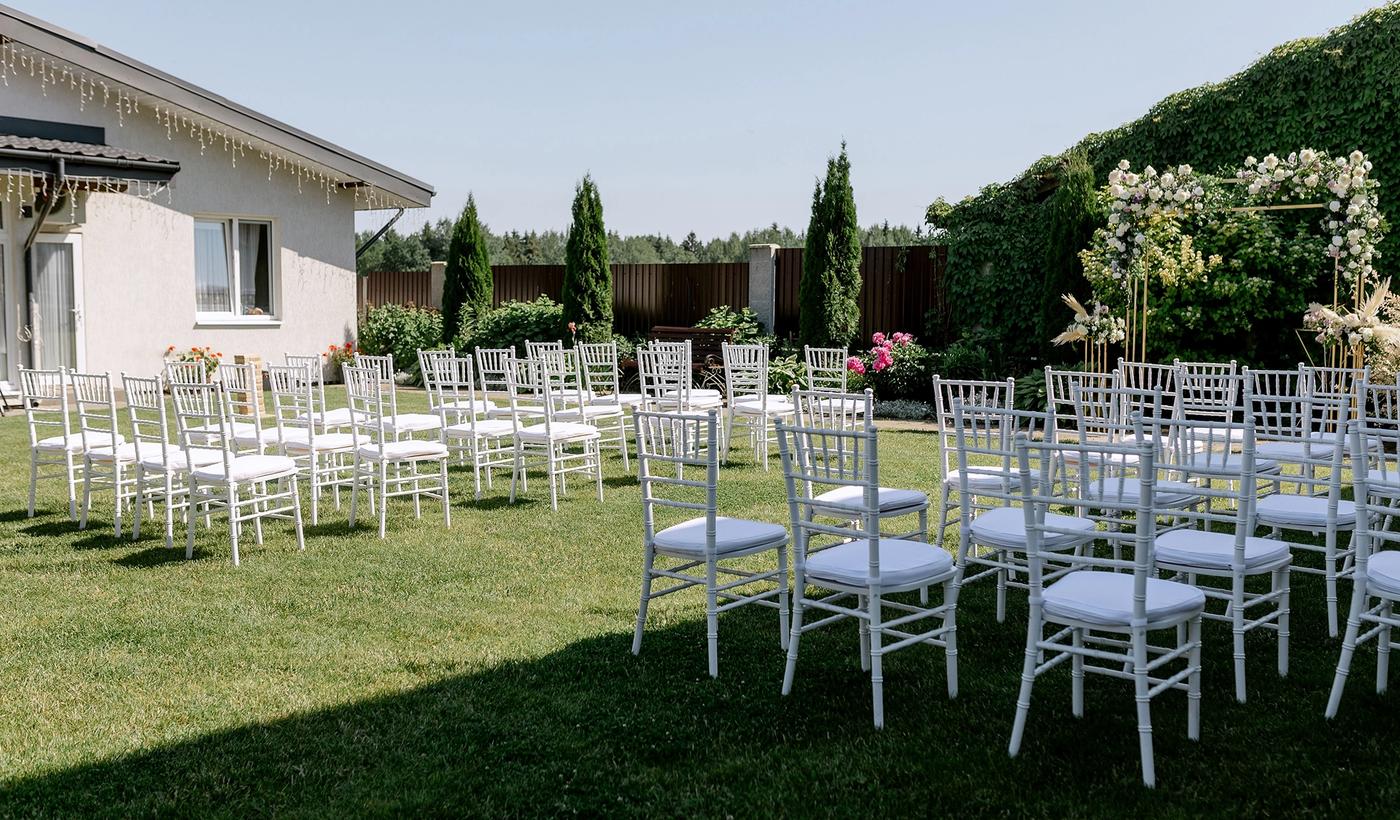 White chairs arranged in a garden setting for an outdoor wedding ceremony