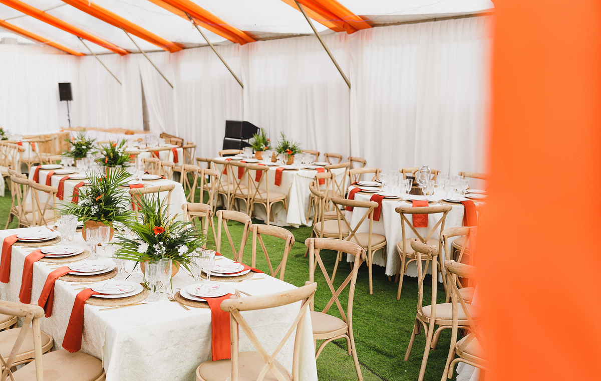 Beautifully arranged event tables with floral centerpieces inside a white and orange tent.