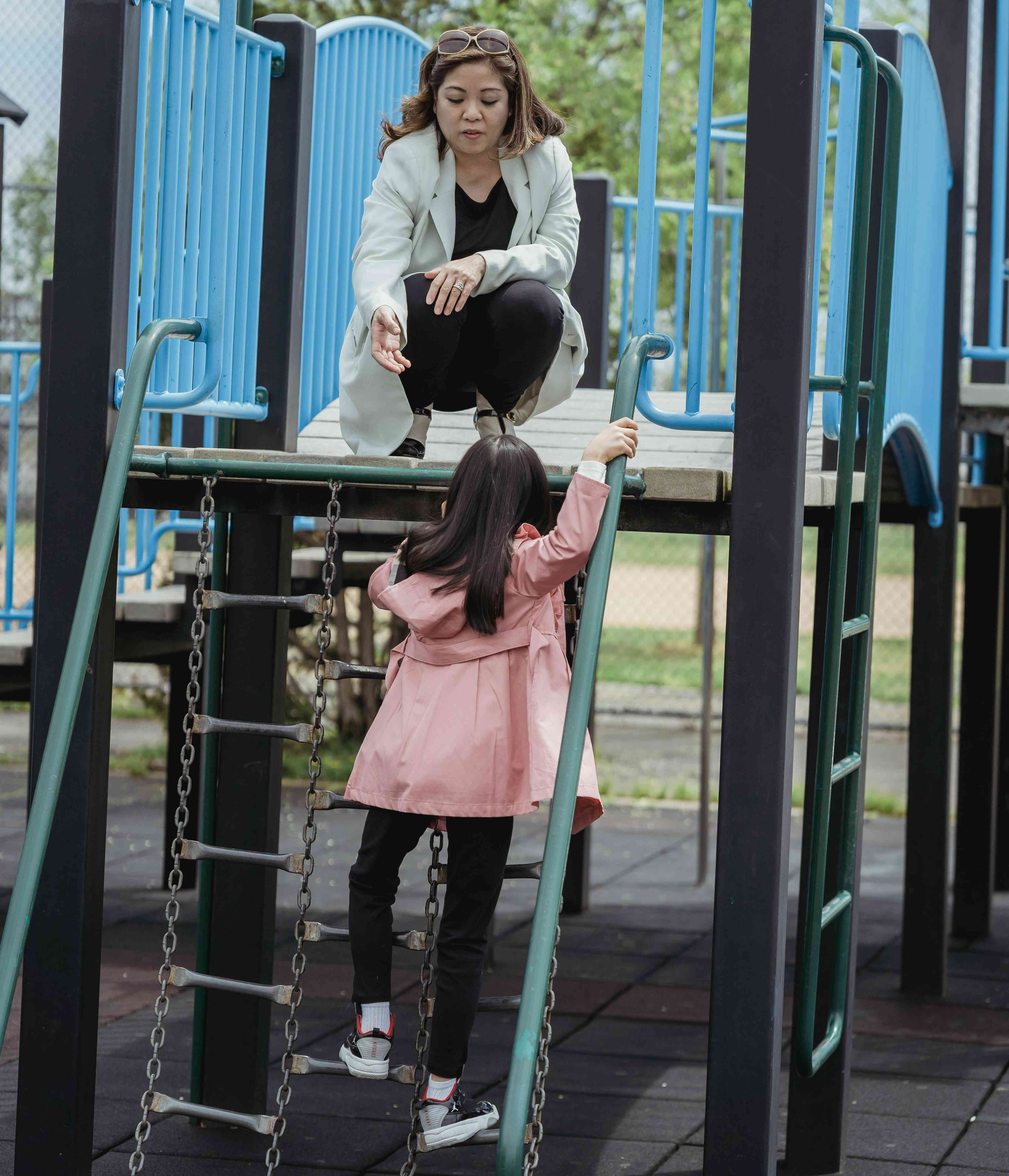 Une femme tend la main à sa fille qui grimpe une échelle en chaîne sur une aire de jeux.
