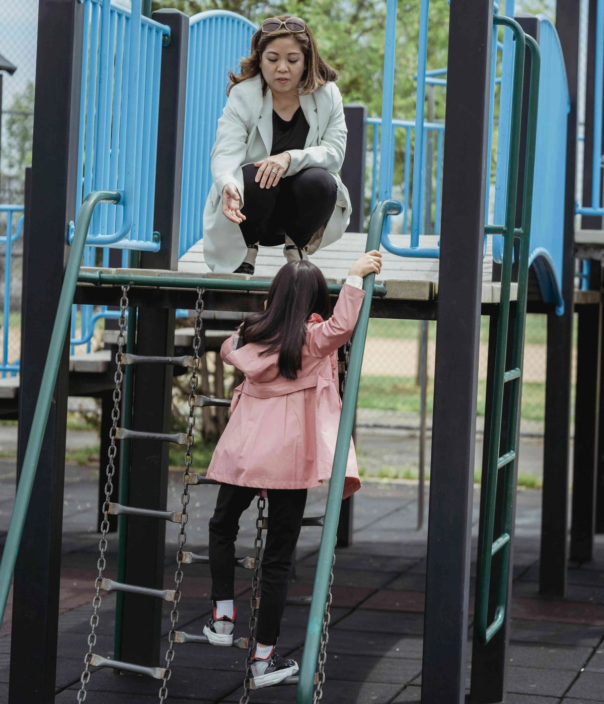 Une femme tend la main à sa fille qui grimpe une échelle en chaîne sur une aire de jeux.