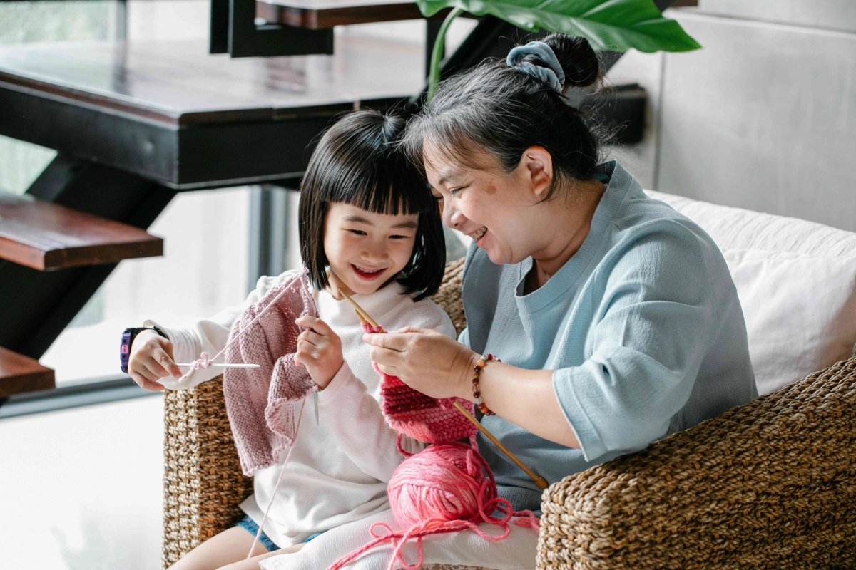 Une grand-mère et sa petite-fille tricotent ensemble dans un fauteuil, transmettant un savoir-faire familial.