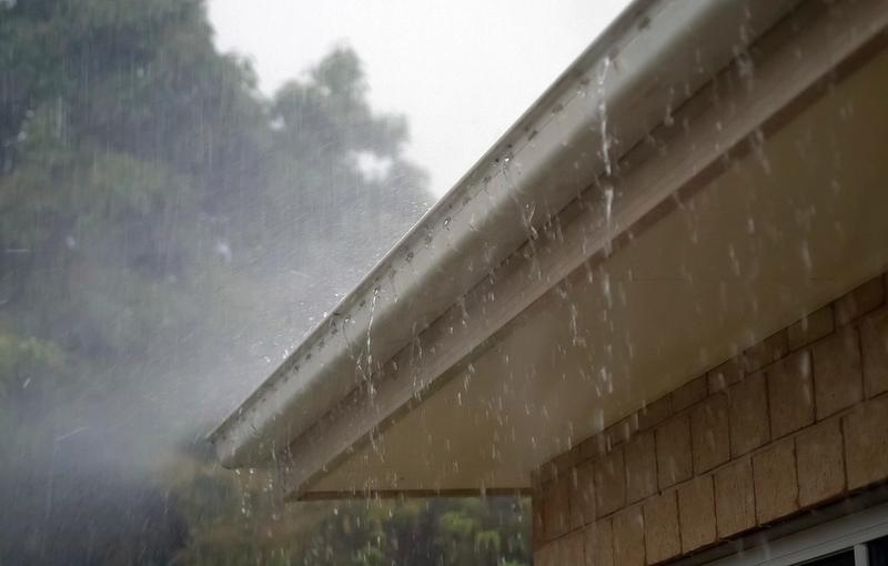 Lluvia intensa cayendo por el borde y la canaleta de un techo