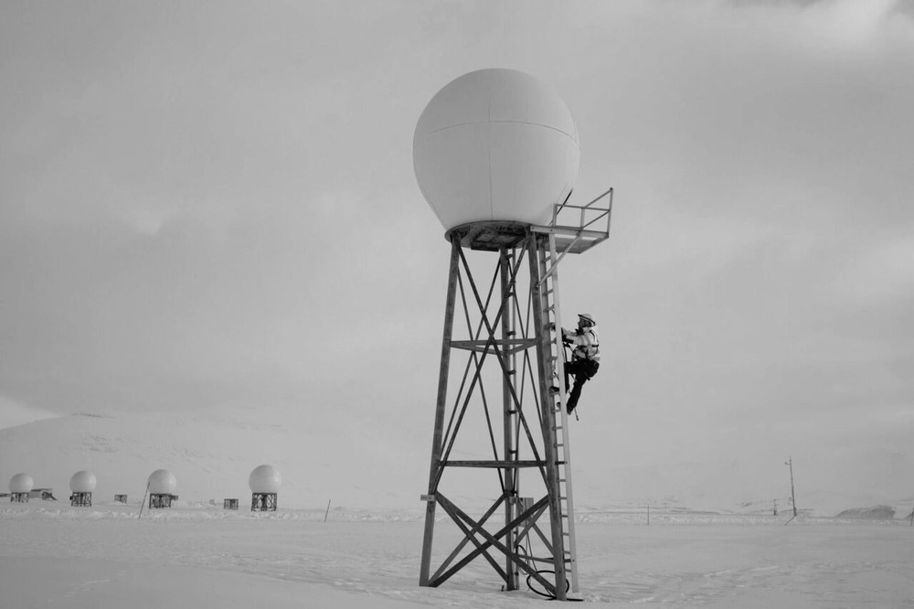 A man climbs a ladder to a spherical weather station in a snowy landscape.