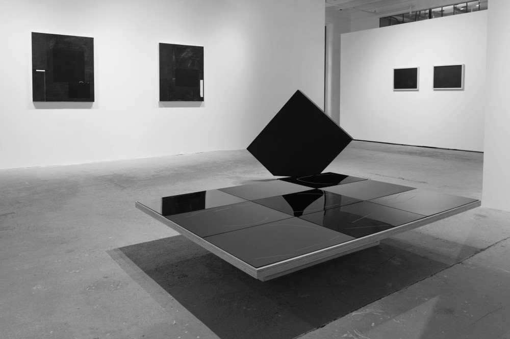 A large, reflective black cube placed at the top right end a of a large dais covered in black tile.