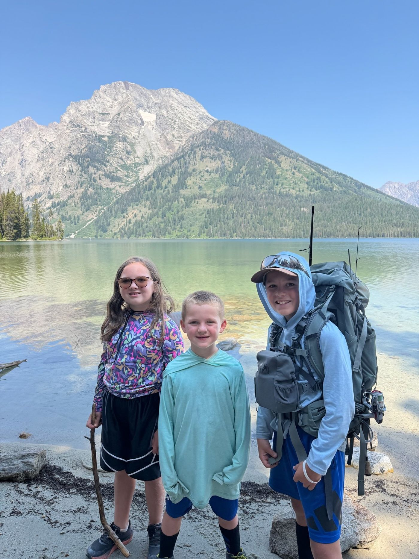 Three children with fishing gear beside a mountain lake.