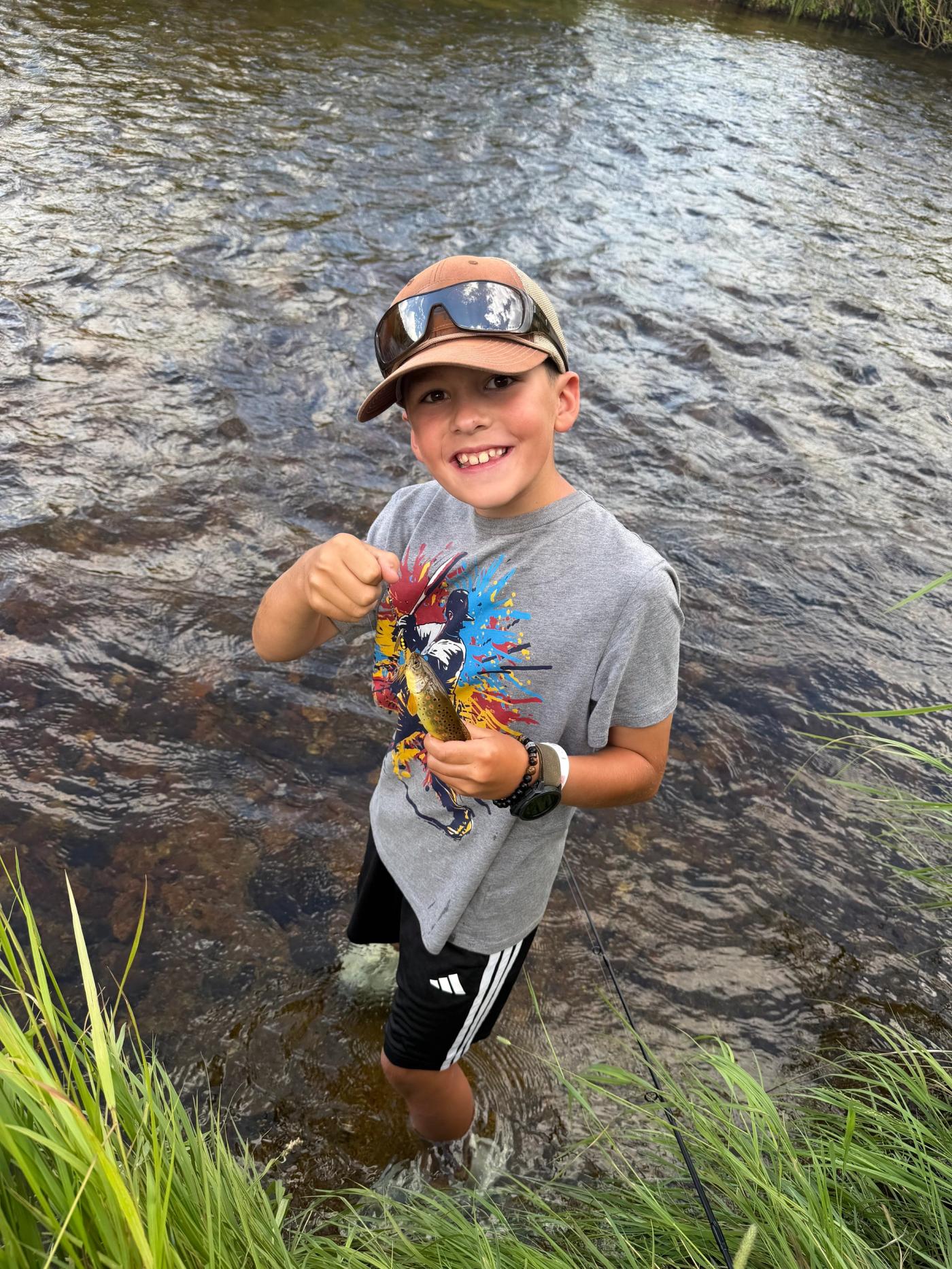 A child holding a small fish beside a stream.