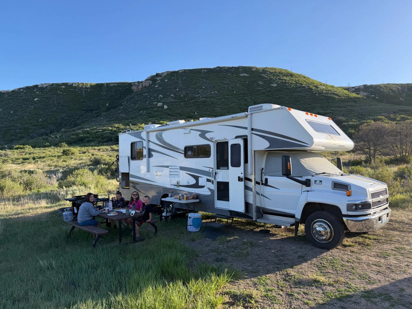 A family eating at a picnic table beside their motorhome.