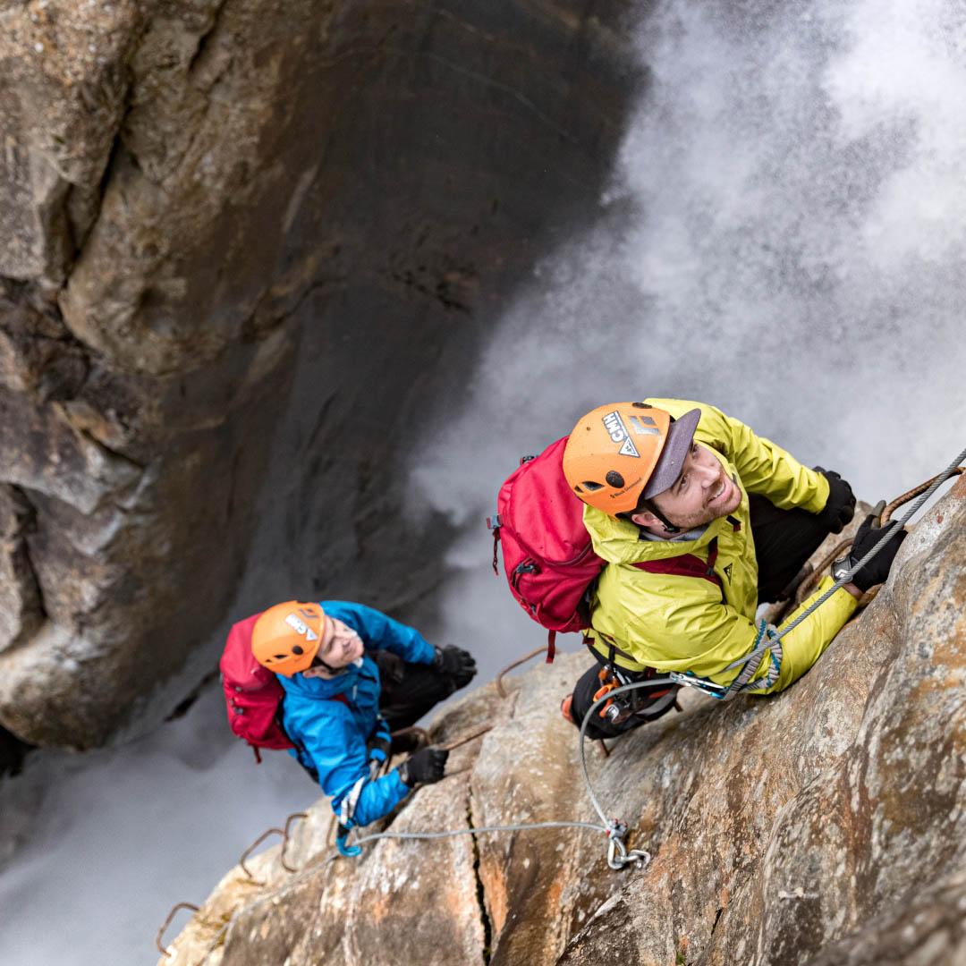 Two men climbing a beside a waterfall