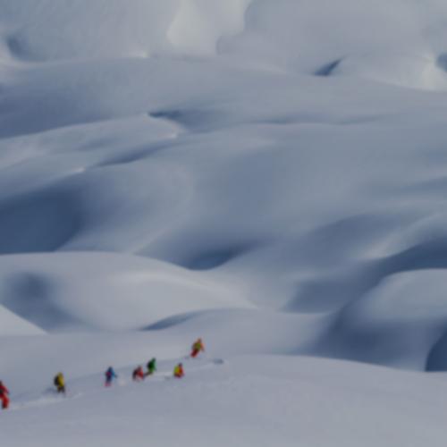 a group of skiers wearing bright jackets are seen in the distance of a dramatic snow covered landscape.