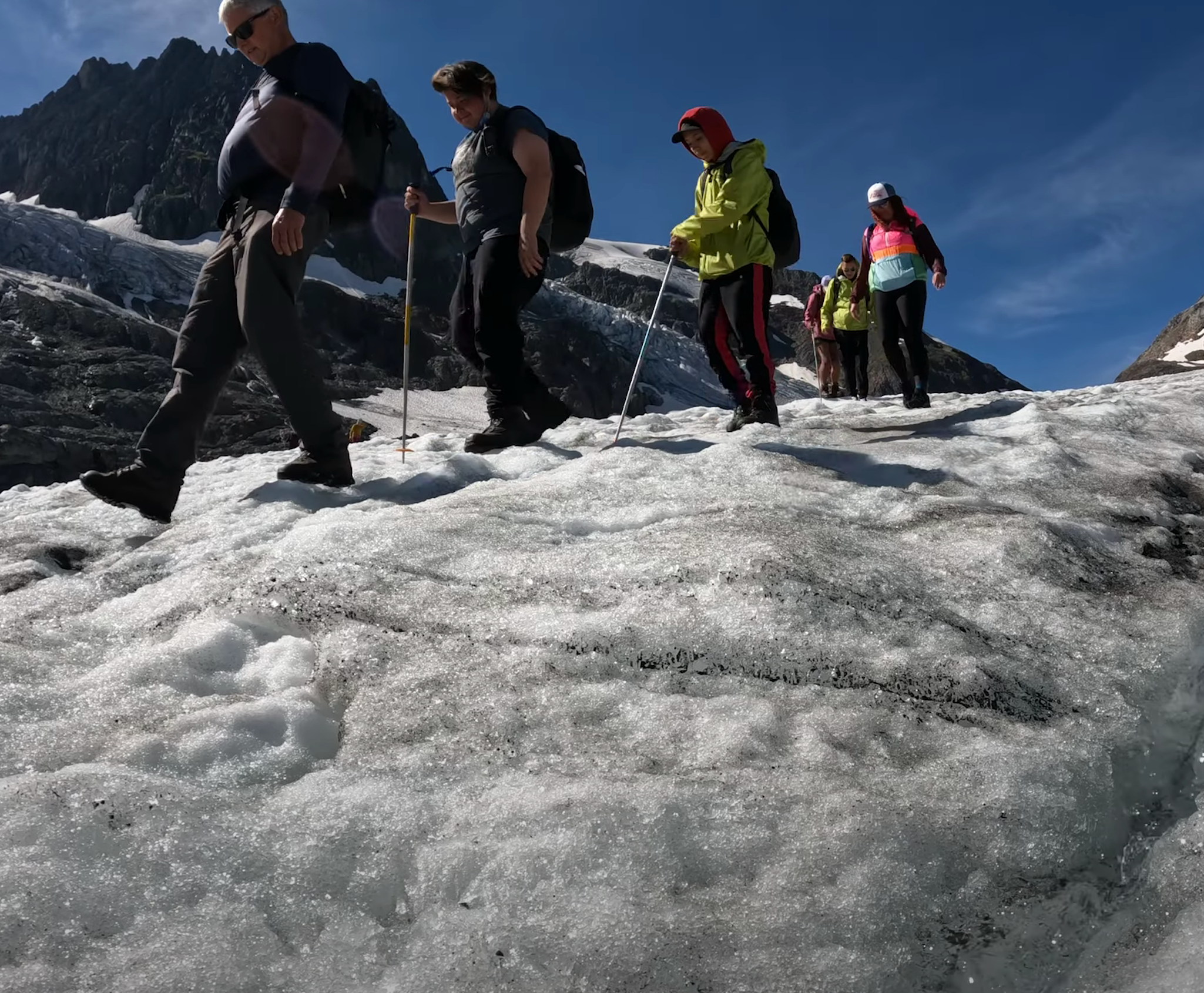 A group of youth hikers follow a mountain guide across a glacier.