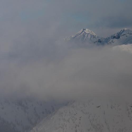 Snow-covered mountain peaks partially hidden by thick clouds and mist.