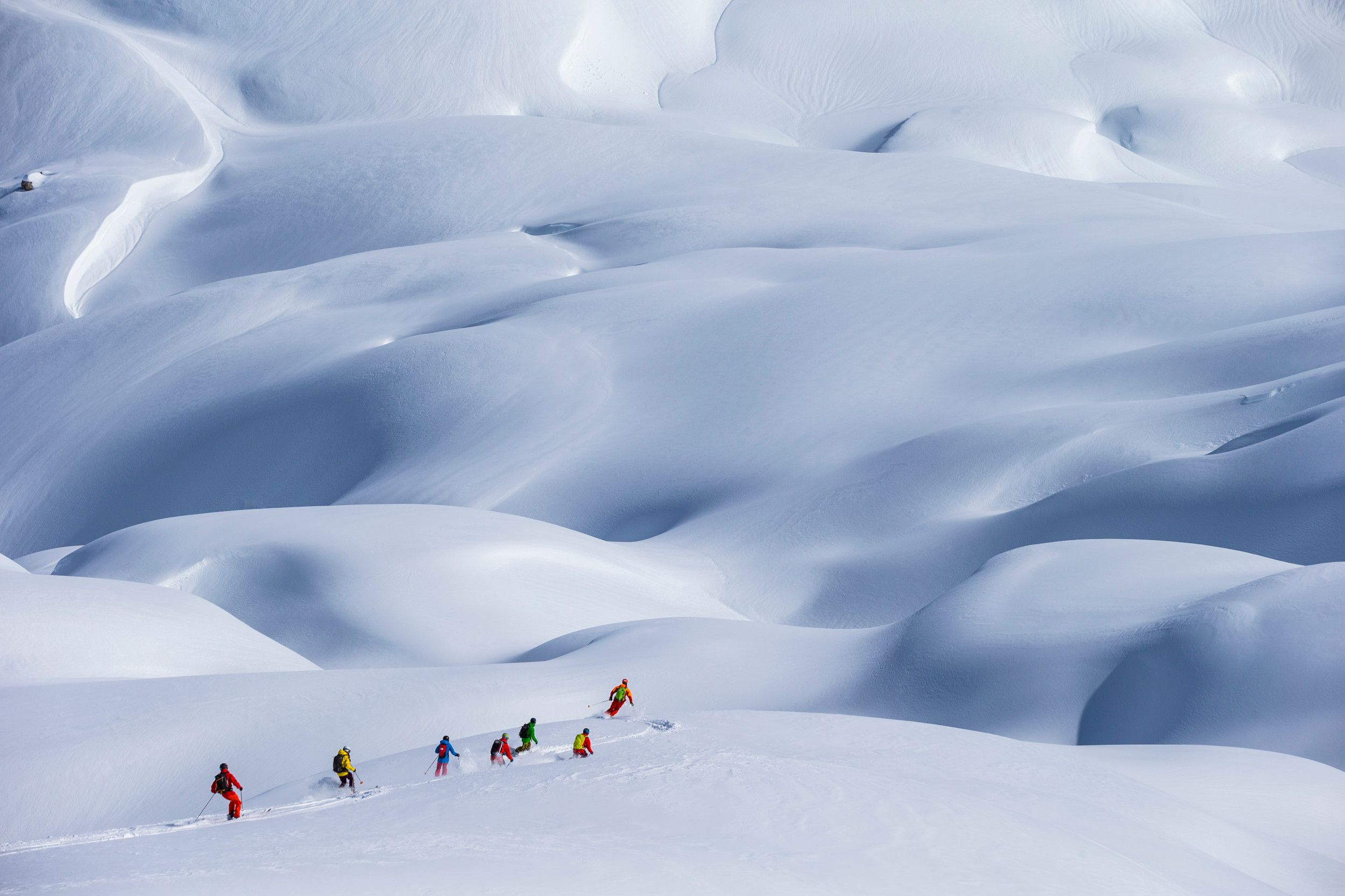 a group of skiers wearing bright jackets are seen in the distance of a dramatic snow covered landscape.