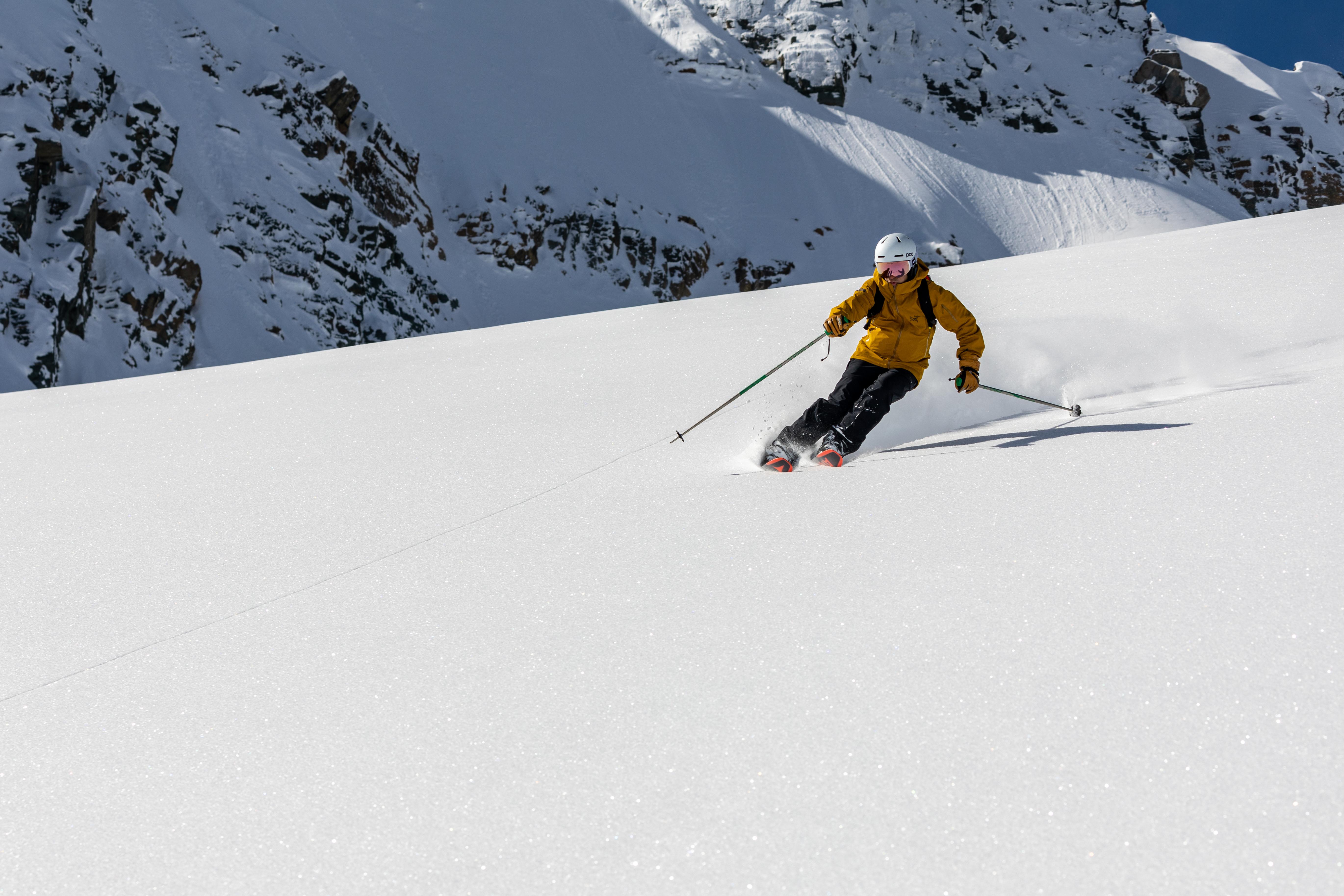 Skier wearing a white helmet and a yellow jacket carving through the snow.