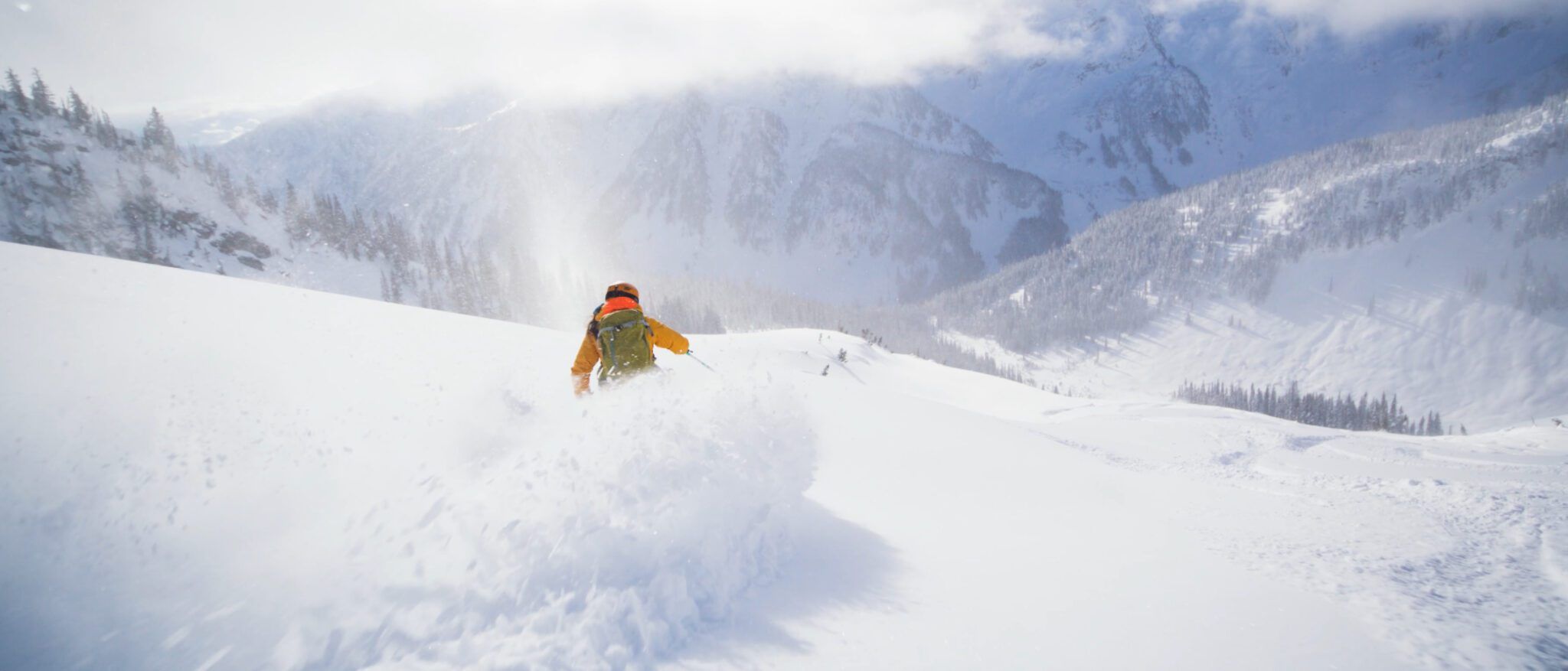 A skier makes a deep powder turn in a sunny alpine bowl.