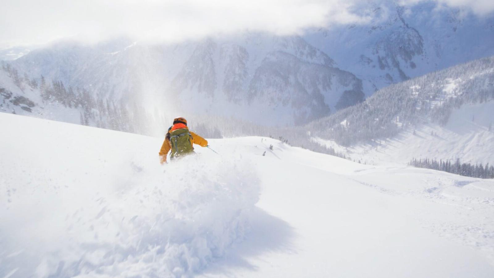 A skier makes a deep powder turn in a sunny alpine bowl.