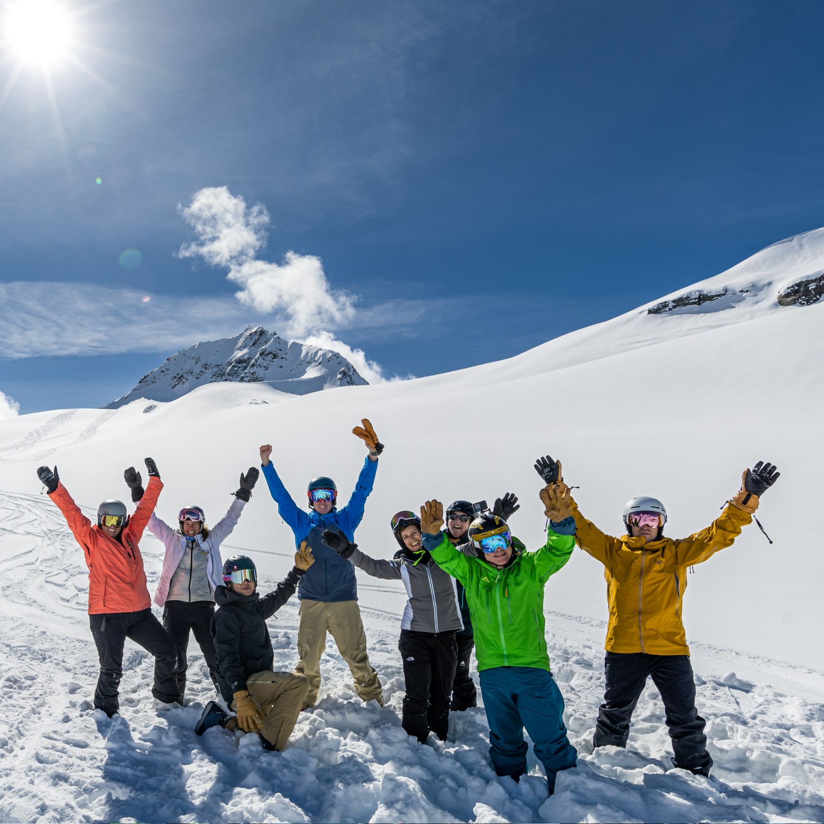 a group of skiers and riders throw there arms up in excitement and smile for the camera.