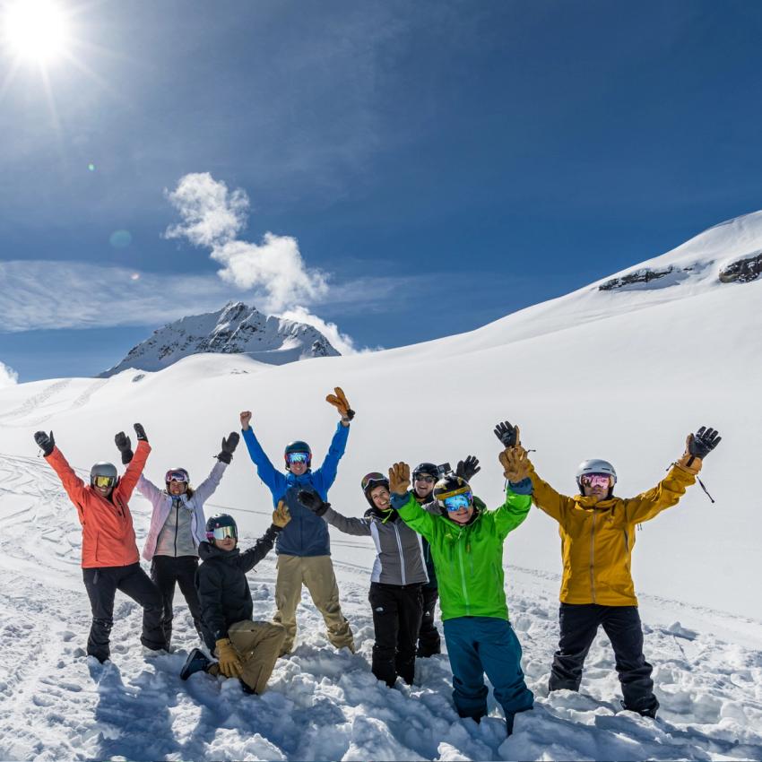a group of skiers and riders throw there arms up in excitement and smile for the camera.