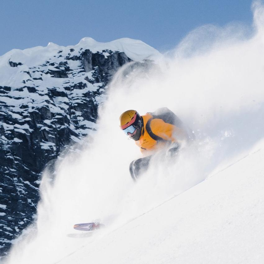 Skier in a yellow jacket skies down a steep slope of deep powder