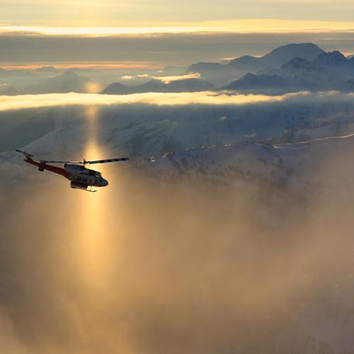 Helicopter flying over sunlit mountains