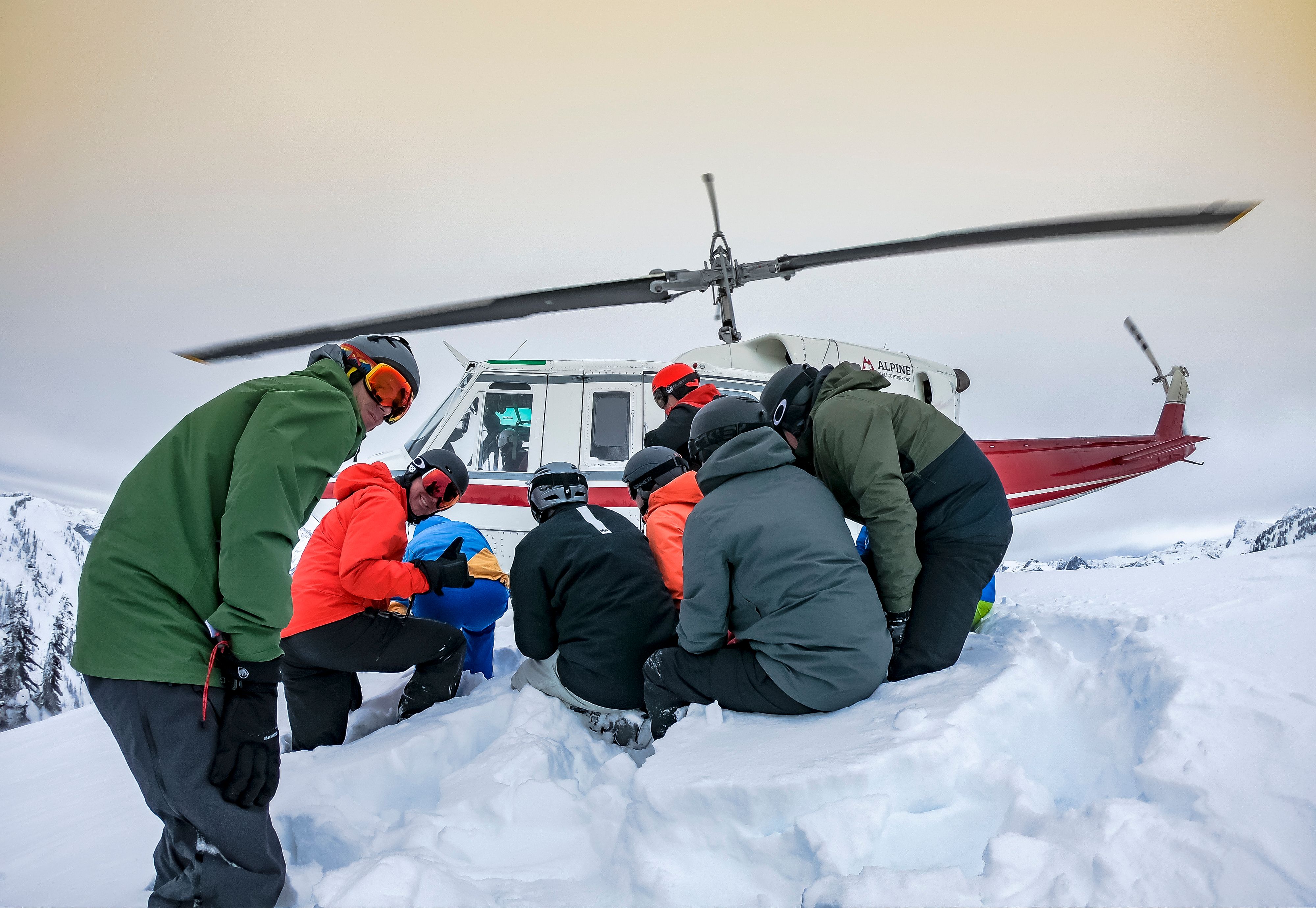 group of heli-skiers gathers around their guide for a safety brief after exiting the helicopter emphasizing the professional protocols of cmh heli-skiing